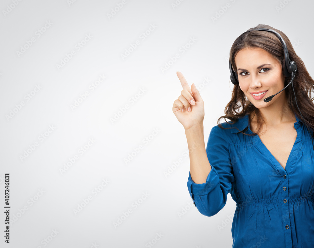 Portrait of happy smiling young support phone operator showing blank copy space area for some text, posing at studio against grey background. Portrait of happy smiling young support phone operator showing blank copy space area for some text, posing at studio against grey background.
