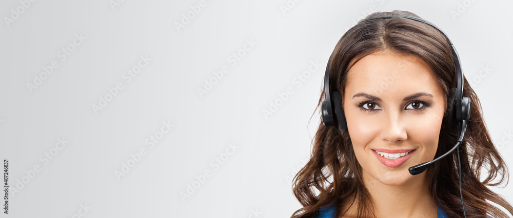 Portrait image of smiling support phone operator or brunette businesswoman in headset, with copy space for slogan or text, at studio picture over grey background Portrait image of smiling support phone operator or brunette businesswoman in headset, with copy space for slogan or text, at studio picture over grey background