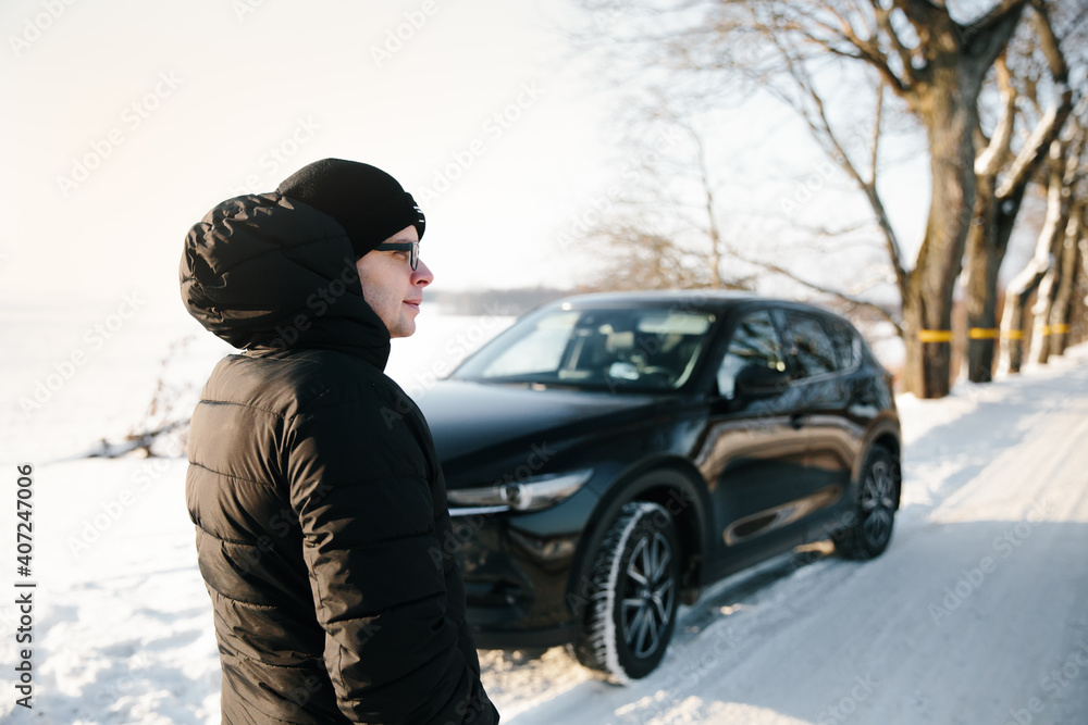 Young man in black stands next to broken car on winter road, waiting for help. Broken car, accident concept. Young man in black stands next to broken car on winter road, waiting for help. Broken car, accident concept.