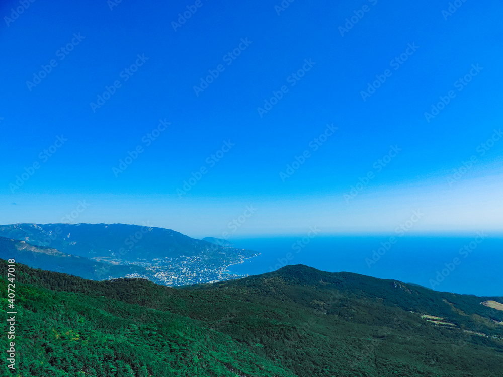 Fototapeta premium Beautiful landscape of green forest hills on the background of blue sea and clear sky.