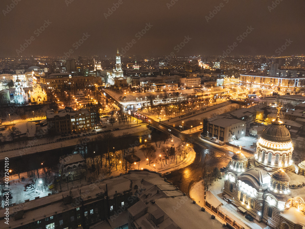 Winter night lights illuminated city aerial view. Holy Annunciation Cathedral, Dormition Cathedral, Serhiivskyi Maidan, Lopan river in Kharkiv, Ukraine