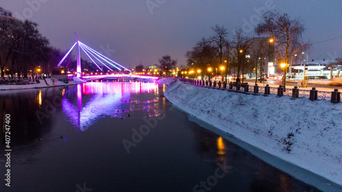 Bridge (Mist Zakokhanykh) across river in illuminated Skver Strilka in Kharkiv city center. Winter aerial evening colorful photo