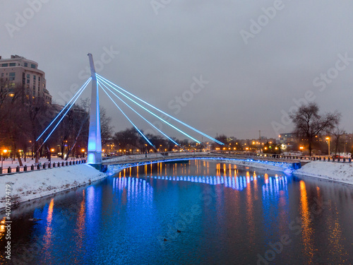 Bridge (Mist Zakokhanykh) across river in blue light illuminated Skver Strilka in Kharkiv city center. Winter aerial evening colorful photo photo