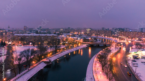 Illuminated evening riverbank with lights reflection in dark water near Skver Strilka in Kharkiv city center. Winter aerial colorful color graded photo