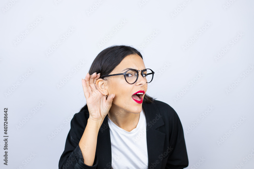 Beautiful business woman surprised with hand over ear listening an hearing to rumor or gossip Beautiful business woman surprised with hand over ear listening an hearing to rumor or gossip