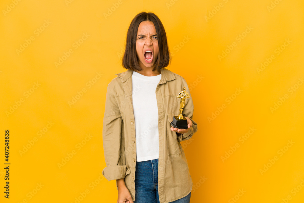 Young hispanic woman holding an award statuette screaming very angry and aggressive. Young hispanic woman holding an award statuette screaming very angry and aggressive.