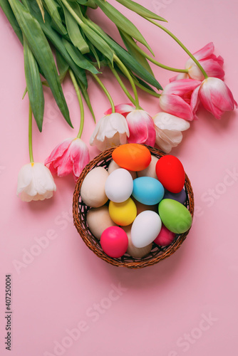 Happy Easter. Pink  white tulips  a basket with colored Easter eggs on a rose background. Vertical photo.