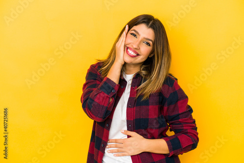 Young indian woman isolated on yellow background laughs happily and has fun keeping hands on stomach.