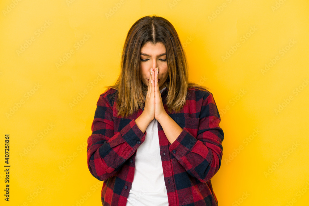 Young indian woman isolated on yellow background praying, showing devotion, religious person looking for divine inspiration. Young indian woman isolated on yellow background praying, showing devotion, religious person looking for divine inspiration.