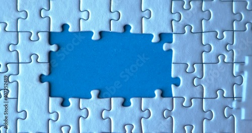 Gray puzzles stacked on blue canvas background. Female hand is putting down pieces. Finishing, completion of work task. Successful achievement of goal. Decision, solution of problem, issue found.