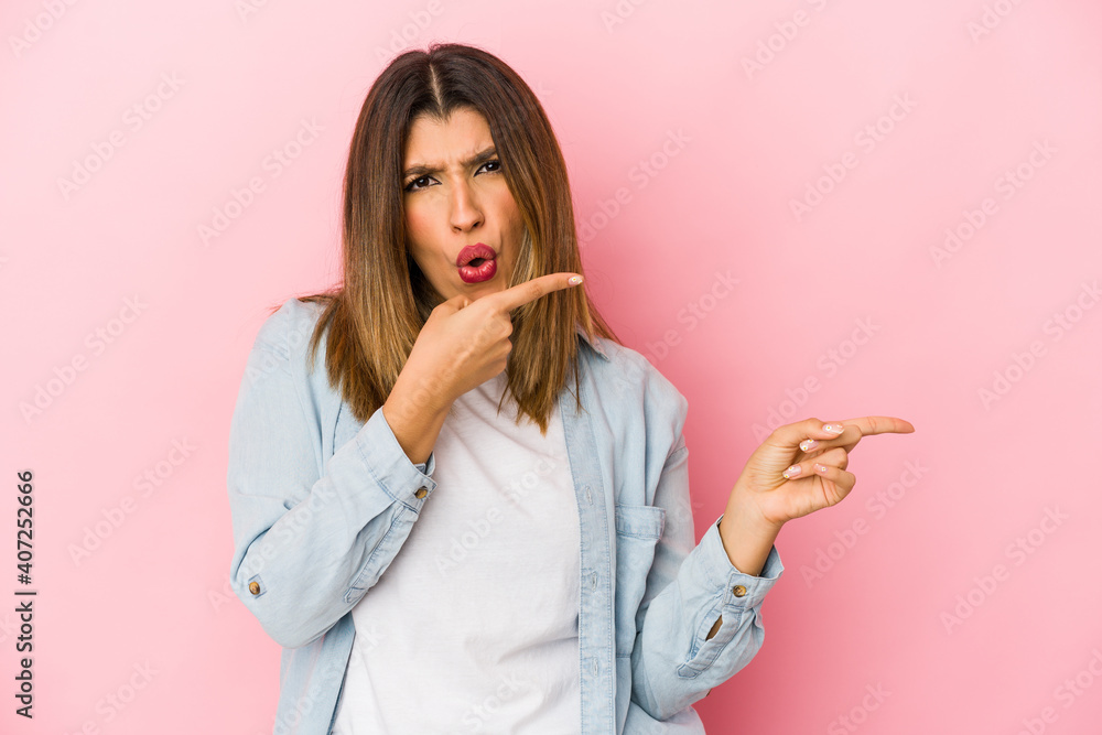 Young indian woman isolated on pink background pointing with forefingers to a copy space, expressing excitement and desire. Young indian woman isolated on pink background pointing with forefingers to a copy space, expressing excitement and desire.