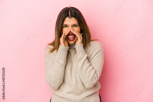 Young indian woman isolated on pink background saying a gossip, pointing to side reporting something.