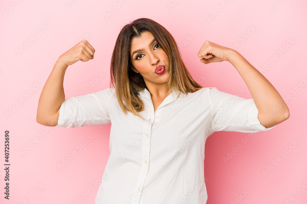 Young indian woman isolated on pink background showing strength gesture with arms, symbol of feminine power