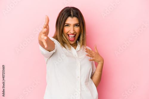 Young indian woman isolated on pink background feels confident giving a hug to the camera.