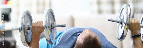 Fotografie A man at home raises heavy dumbbells from a prone position