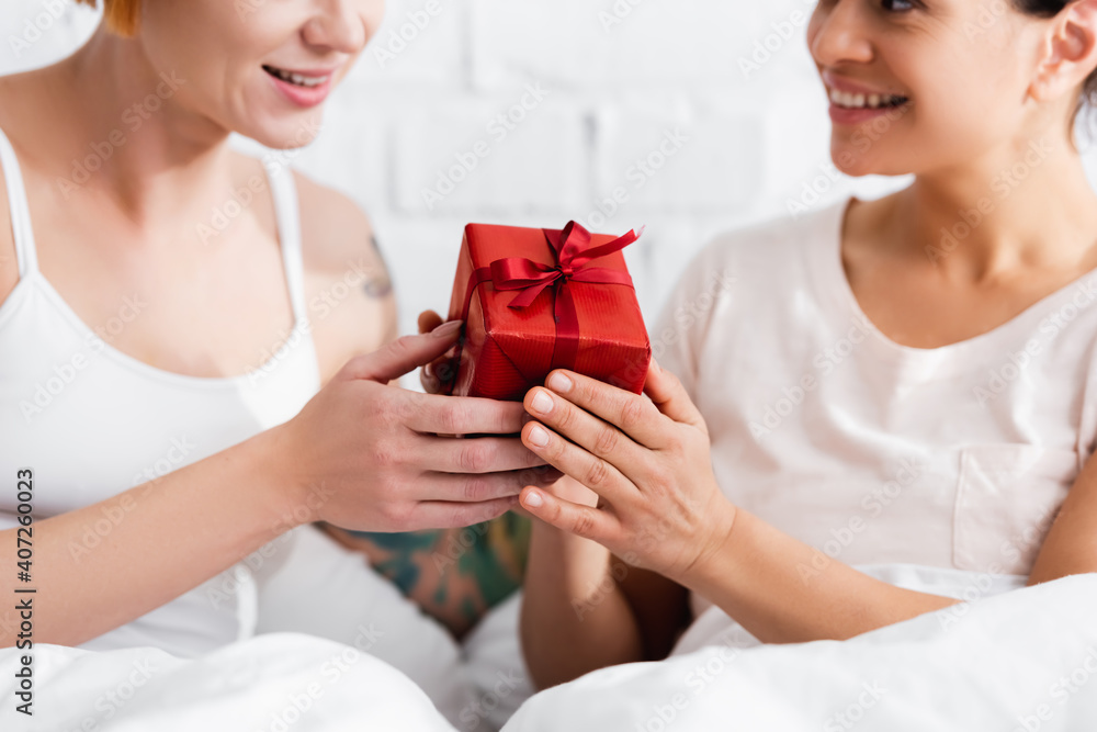 cropped view of african american woman presenting gift to lesbian girlfriend in bedroom cropped view of african american woman presenting gift to lesbian girlfriend in bedroom