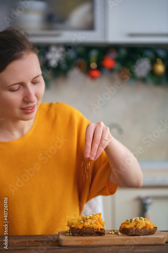 woman sprinkles sesame seeds on delicious baked pumpkin sandwiches.