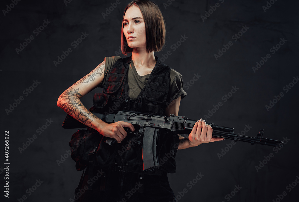 Dressed in dark armour military woman with short haircut and bandaged hand holds her assault rifle in dark smokey background. Dressed in dark armour military woman with short haircut and bandaged hand holds her assault rifle in dark smokey background.