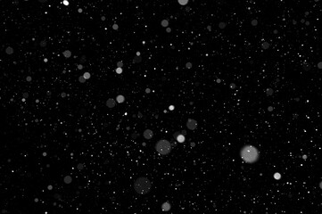 Bokeh of white snow on a black background. Falling snowflakes on night sky background, isolated for post production and overlay in graphic editor.