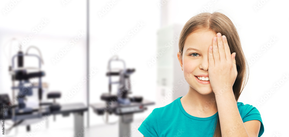 Smiling teen girl closing eye with her hand for checking vision, over background ophthalmology clinic. Vision test concept Smiling teen girl closing eye with her hand for checking vision, over background ophthalmology clinic. Vision test concept