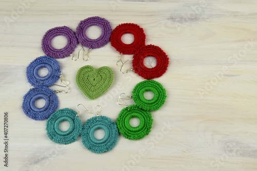 Colorful crochet earrings laying on cirlce and green heart, crocheted jewllery on white wooden background, women's hobby, crocheting photo