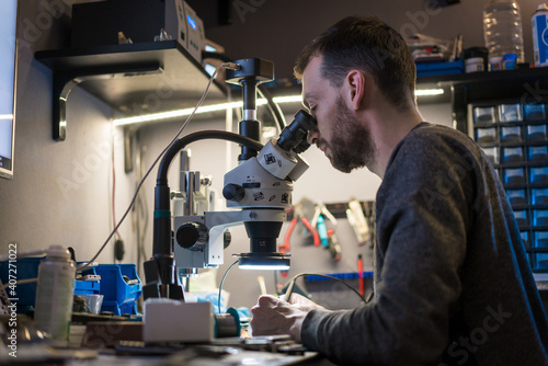 Handsome young man using microscope for fixing and repairing microchips microsoldering soldering concept worker