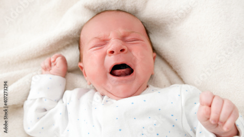 Closeup portrait of newborn baby crying and screaming while lying in crib