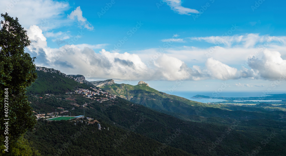 Panoramic view of landscape of Supramonte mountains with green soccer field at Baunei village, limestone rocks, Arbatax cape, mediterranean sea and lush vegetation. Sardinia, Italy