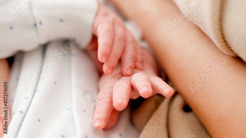 Closeup of little newborn baby hands while sleeping on young caring mother