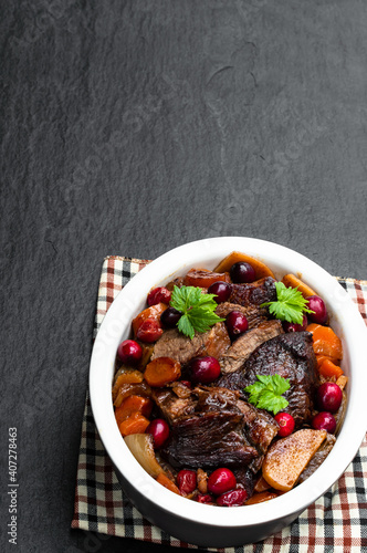 Braised beef with cranberries in clay bowl on black stone background