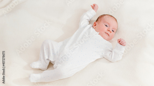 Top view on adorable newborn baby in white bodysuit lying on bed and looking on bright sun. Newborn babies at home