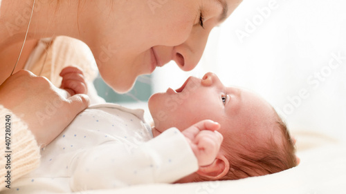 Closeup shot of beautiful young mother cuddling and stroking her little baby son lying on bed in sun light. Concept of family happiness and loving parents with little children