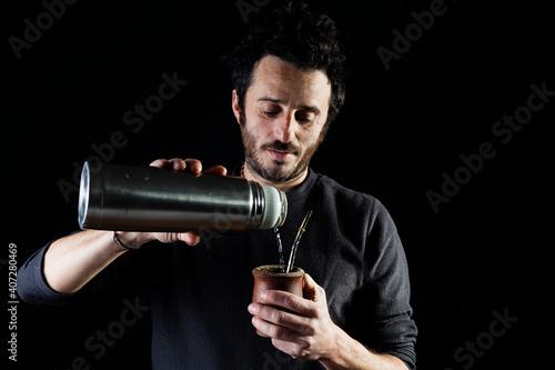 Close up shot of adult man pouring hot water from a thermo on a  yerba mate container, this traditional south and central american herb mixture with negative space and black background. photo