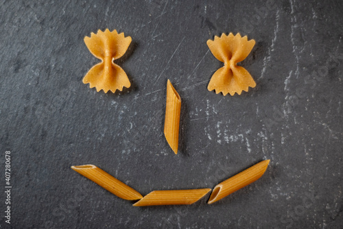 Wholemeal pasta. Pasta used to compose a smiley face on a slate dish. Healthy nutrition concept