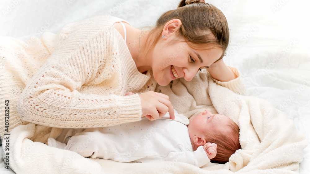 Portrait of happy smiling woman with little newborn baby lying on soft bed at morning Portrait of happy smiling woman with little newborn baby lying on soft bed at morning