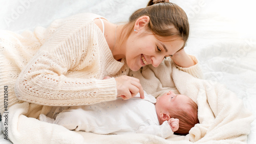 Portrait of happy smiling woman with little newborn baby lying on soft bed at morning