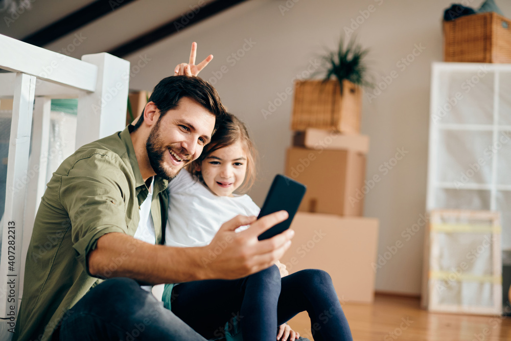 Happy father taking selfie with his playful daughter at their new apartment. Happy father taking selfie with his playful daughter at their new apartment.