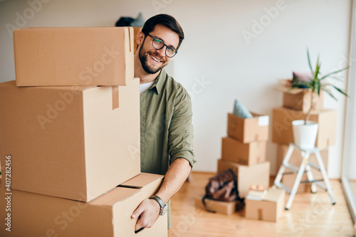 Happy man carrying stack of cardboard boxes while relocating in a new apartment. photo