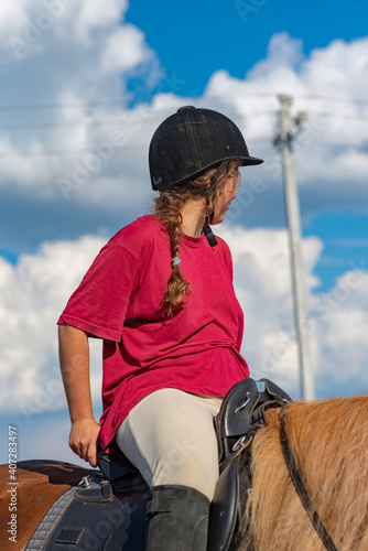 A young beautiful girl in a jockey cap and a red T-shirt rides a horse.