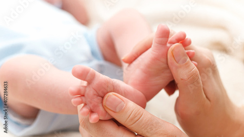 Closeup of young caring and loving mother massaging and stroking little feet of her newborn baby son lying in bed. Concept of family happiness and loving parents with little children. Baby massage and © Кирилл Рыжов