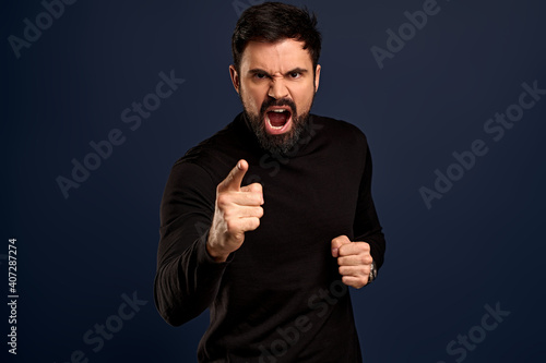 Man threatening person with angry outraged expression, lose temper standing distressed, pointing camera accuse someone, blame girlfriend, having argument and shouting, Blue background
