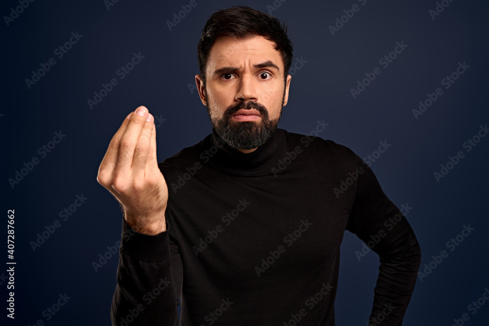 Fototapeta premium Where is my money. Serious-looking confident young bearded businessman in high neck sweater, showing cash gesture, rubbing fingers against each other and smirk displeased, someone own him