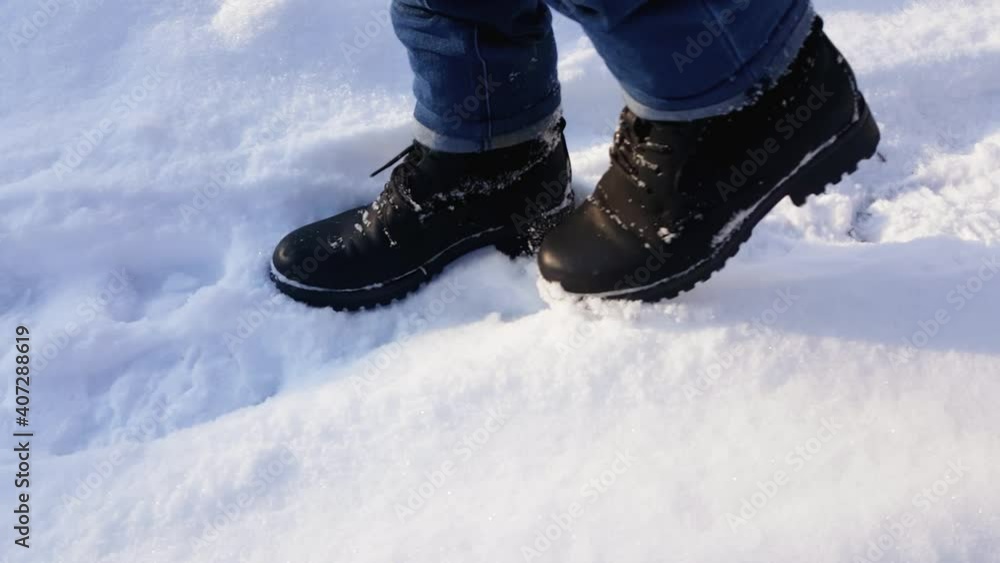 Feet of a woman walking in the snow on a snowy day in black boots and blue jeans. Side view. Walk in the snowy city. Feet of a woman walking in the snow on a snowy day in black boots and blue jeans. Side view. Walk in the snowy city.