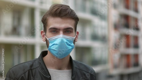 Young handsome man takes off his medical protective face mask and drinks mineral water from big plastic bottle. Cinema 4K panoramic slow motion video photo