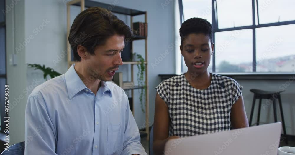 Diverse business colleagues sitting at desk using laptop going through paperwork in office Diverse business colleagues sitting at desk using laptop going through paperwork in office
