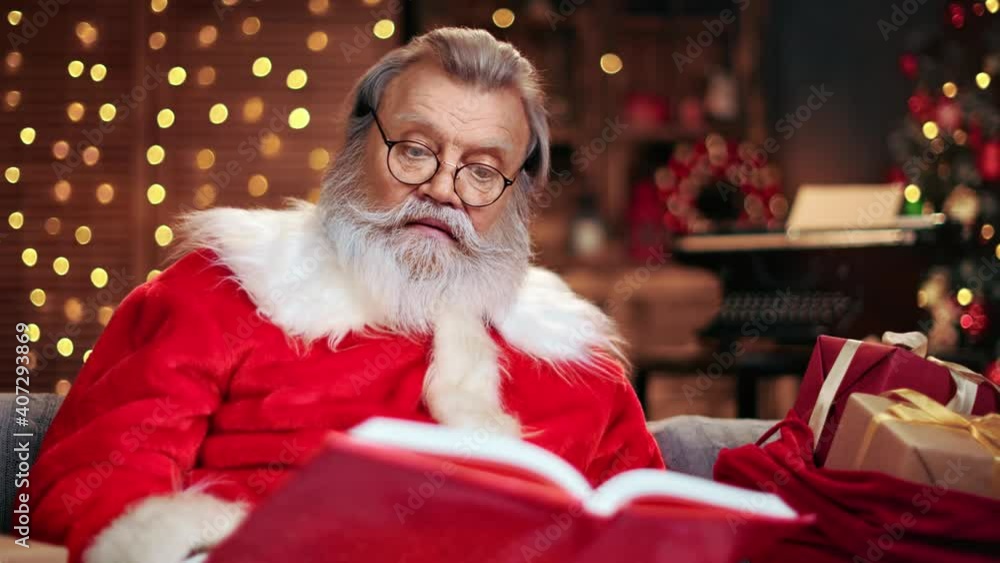 Pensive male Santa Claus attentively reading red book of Christmas wishes. 4k Dragon RED camera Pensive male Santa Claus attentively reading red book of Christmas wishes. 4k Dragon RED camera