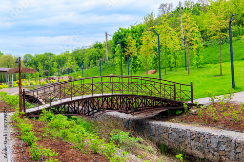 Beautiful view of the city park with arched footbridge across small river and young trees