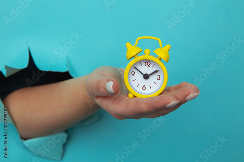 Fototapeta Naklejka Na Ścianę i Meble -  Woman hand holds yellow alarm clock through a paper hole. Time management and deadline concept.