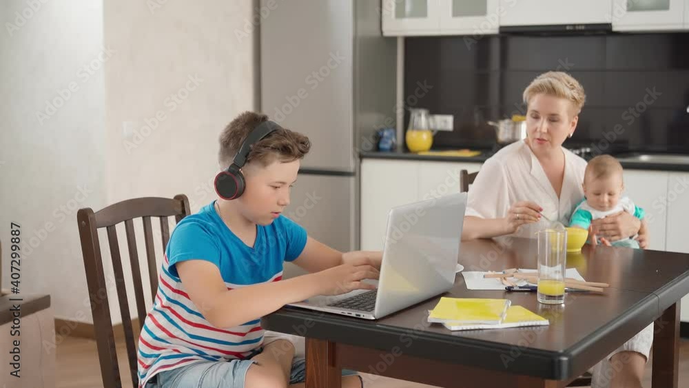 Mother feeding little son while eldest playing on laptop Mother feeding little son while eldest playing on laptop