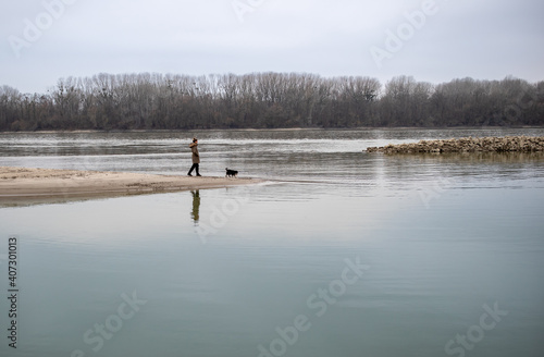 Girl with dog walking on river coast on cold day
